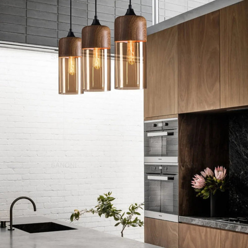 Three Jasper slim cylinder woodgrain and amber glass pendant lights above a kitchen island