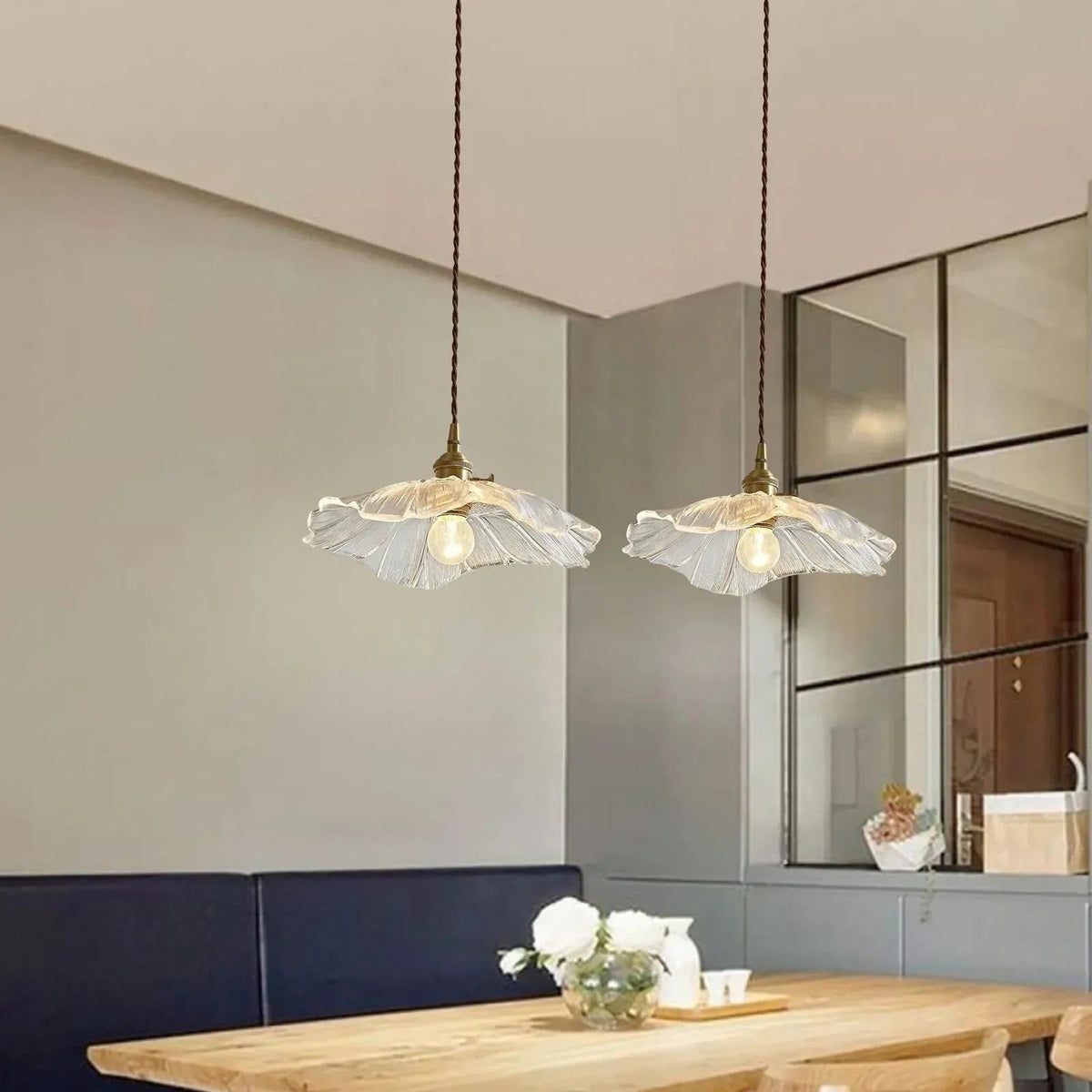 Pair of clear flower glass pendant lights above a dining table and bench