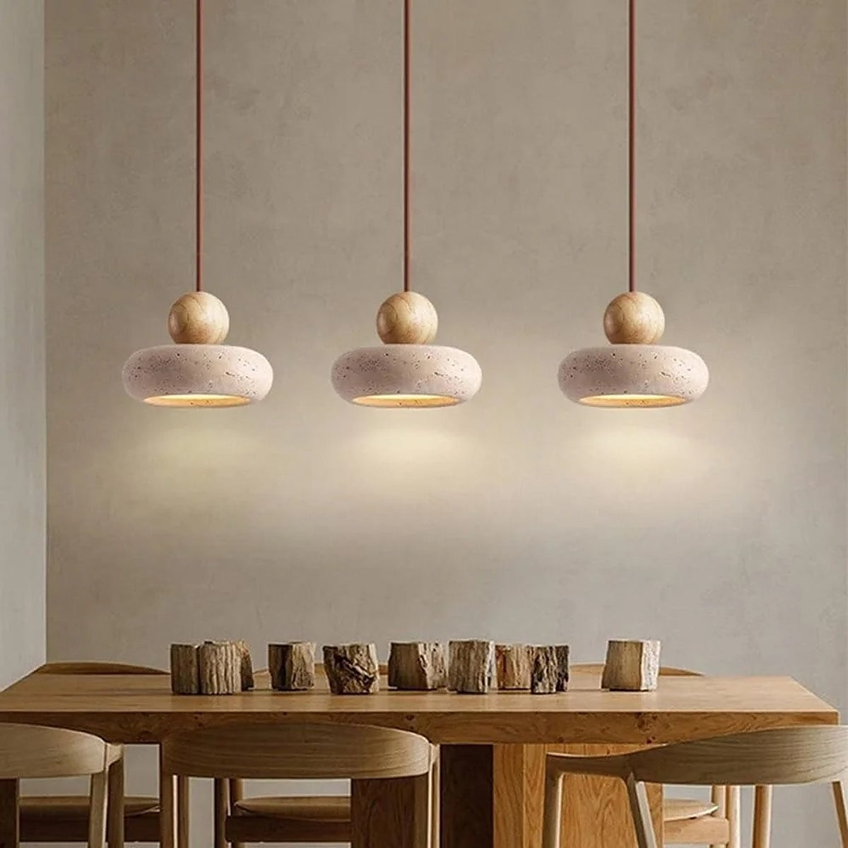 Three Orin travertine and light wood pendant lights above a timber dining table